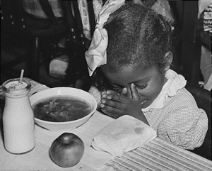 Young girl prays before eating a school meal with milk during the Great Depression.